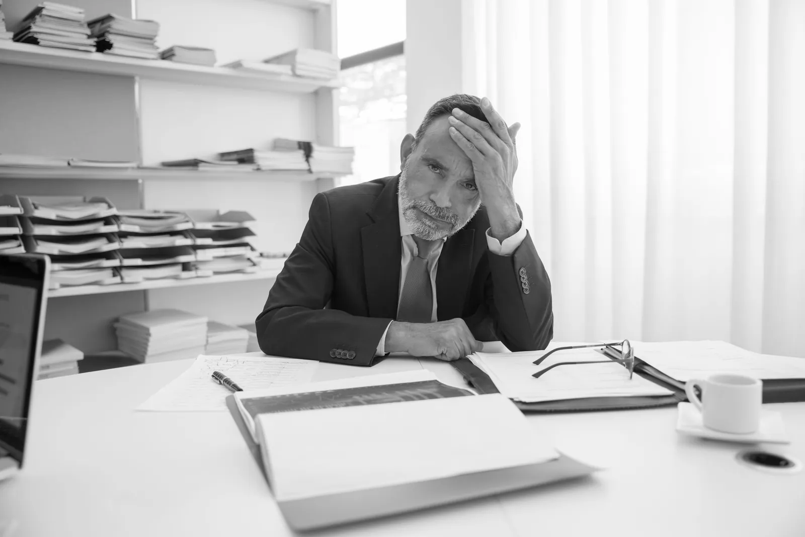 A law firm partner in a suit at his desk, hand on his head over open case files